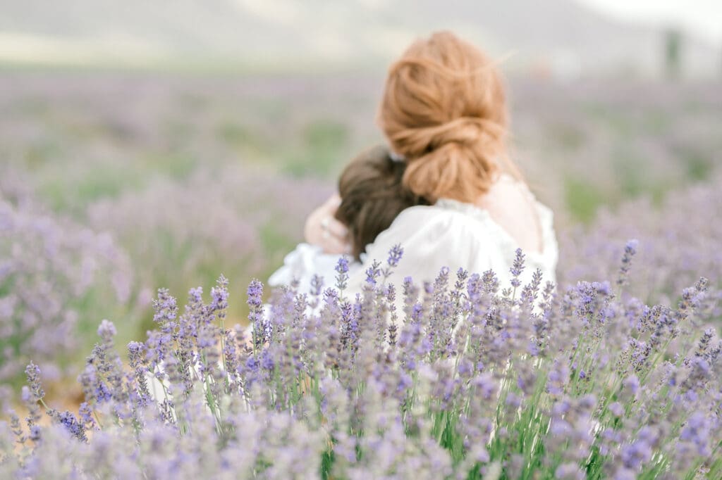 mom holding daughter while sitting amongst the lavender flowers