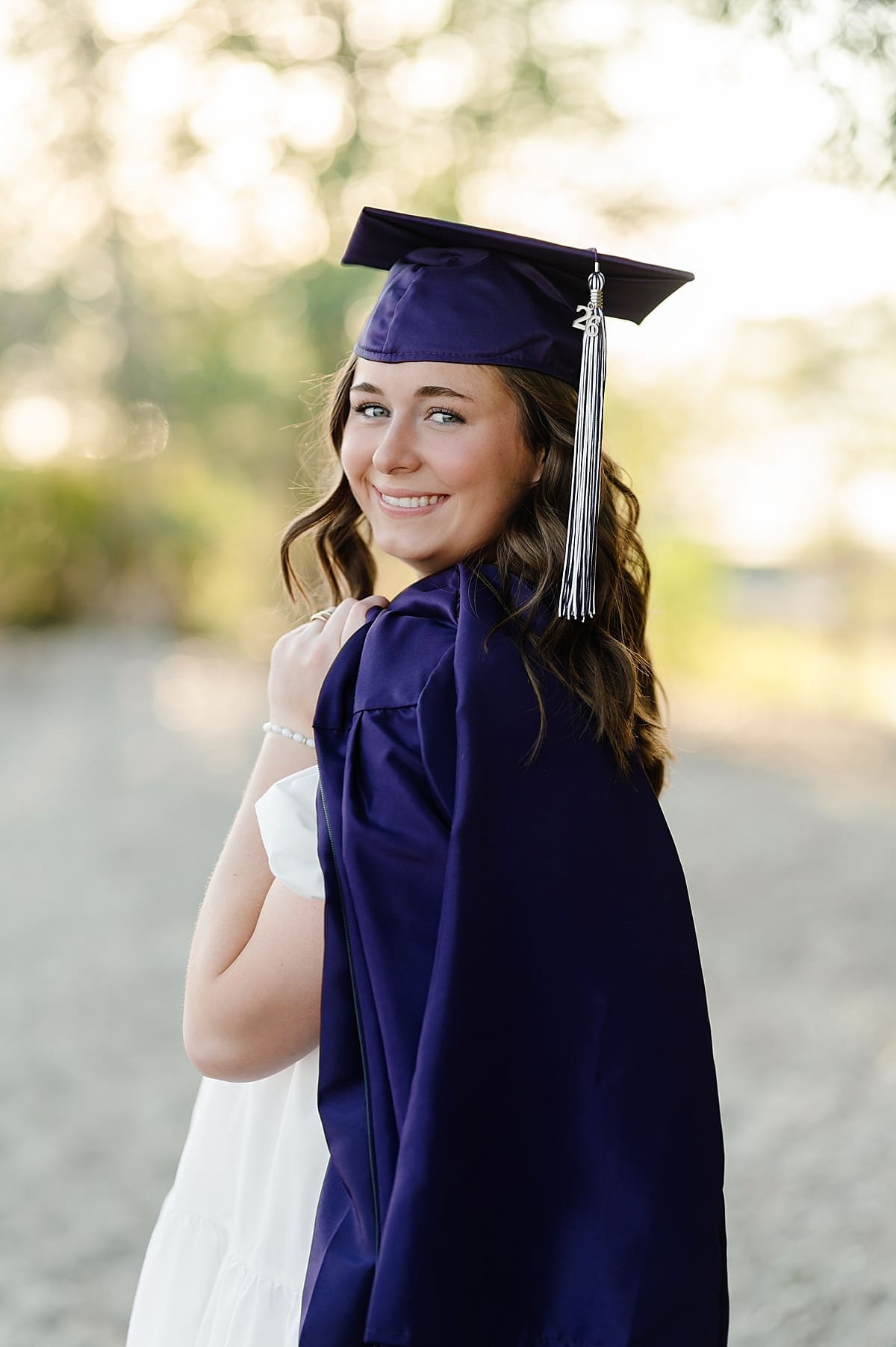 Senior girl with cap and gown looking back over her shoulder smiling at the camera with Heidi Burton Photography